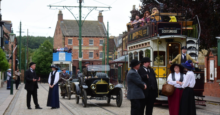 The 1900s Town street at Beamish Museum filled with people in period costume and visitors sat on an historic tram.